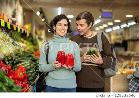 Married couple selects fresh bell peppers, tomatoes and other vegetables at supermarket counter Married couple selects fresh bell peppers, tomatoes and other vegetables at supermarket counter 129538646