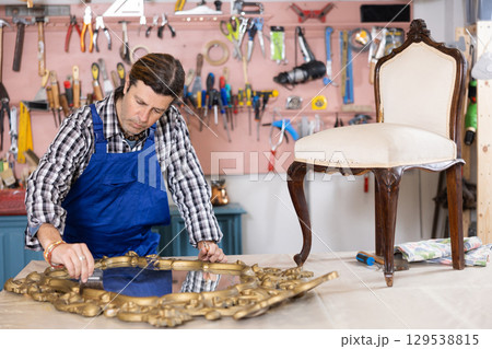 Male carpenter working on restoring vintage mirror in workshop 129538815