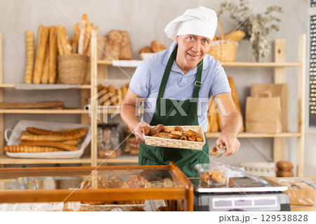 Elderly male seller puts pastry croissant in plastic package, put on scales, sets price of product Elderly male seller puts pastry croissant in plastic package, put on scales, sets price of product 129538828