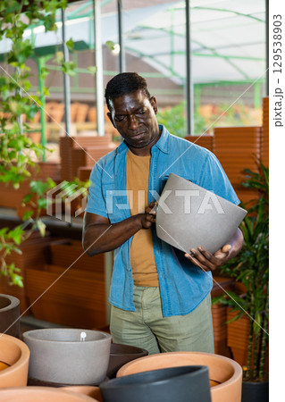 African american man chooses flower pots for indoor plants 129538903