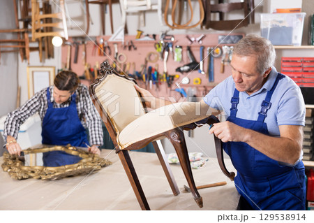 To replace upholstery, restorer removes old cloth seat covering from antique wooden chair. 129538914