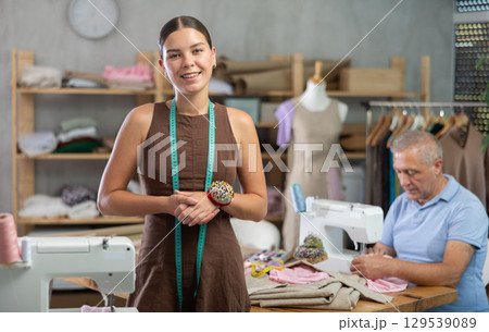Young woman posing male assistant sewing in workshop 129539089