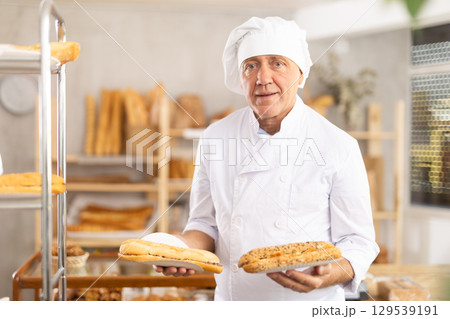 Elderly man chef of pastry shop demonstrates product of assortment, bocadillo on disposable plates 129539191
