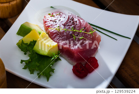 Delicious pieces raw tuna, green avocado and greens at plate 129539224