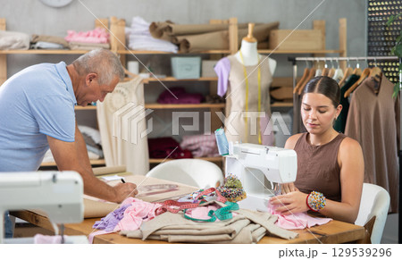 Young woman sewing male assistant drawing pattern on paper 129539296