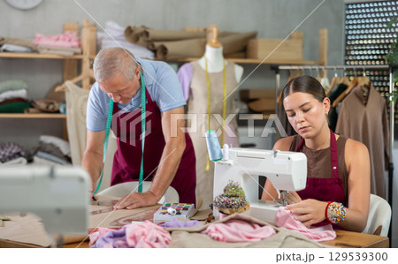 Girl master sew clothes in sewing machine, senior craftsman draw dress pattern 129539300