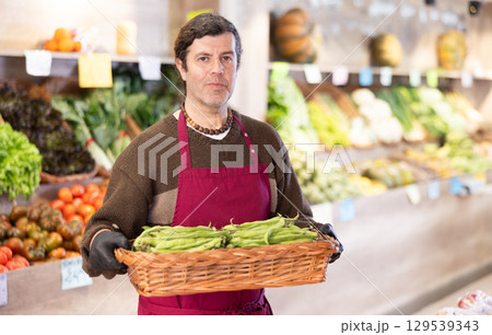Man salesperson carries large basket of beans in pods from warehouse to sales area in shop Man salesperson carries large basket of beans in pods from warehouse to sales area in shop 129539343