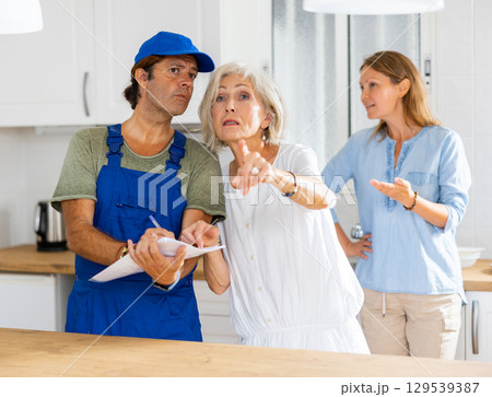 Mature housewife tells the plumber where to change the pipes in kitchen 129539387