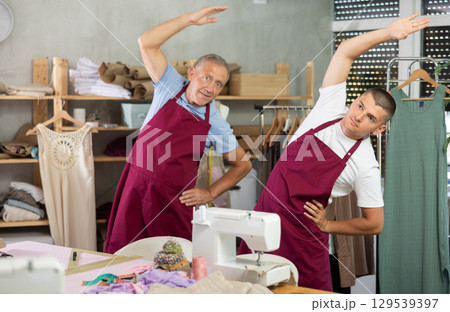 Elderly and young man doing warm-up exercises in sewing workshop 129539397