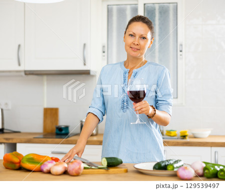 Woman with glass of wine in kitchen Woman with glass of wine in kitchen 129539497