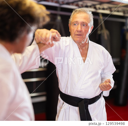 Older karate fighter practicing paired kumite in dojo Older karate fighter practicing paired kumite in dojo 129539498