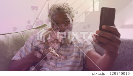 Image of falling hearts over african american senior man using smartphone 129540019