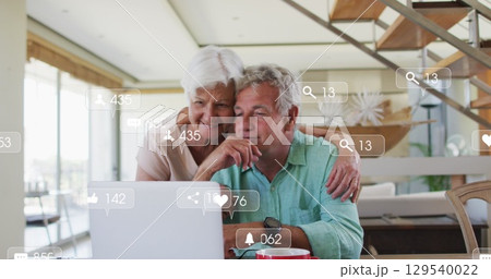 Image of falling icons over caucasian senior couple using laptop Image of falling icons over caucasian senior couple using laptop 129540022