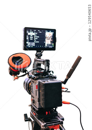 Professional digital video camera with external monitor and accessories, mounted on a tripod. The camera is equipped with a lens and an external battery. Video camera on a white background, isotyat. 129540653