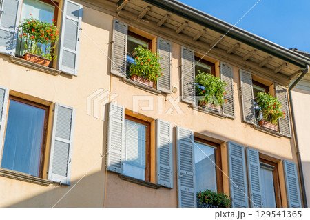 Windows with wooden shutters. Flowers on the windowsill in summer. Italian style facade. Wall Windows with wooden shutters. Flowers on the windowsill in summer. Italian style facade. Wall 129541365