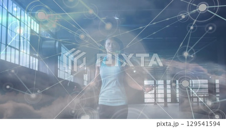 Image of network of connections over clouds and fit afrcian american woman jumping 129541594