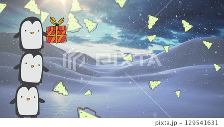 Balancing penguins stacking in snowy hills, with gift box, suitcase holding tree shapes, copy space 129541631
