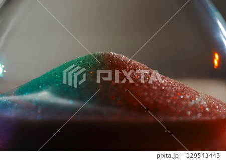 Rainbow sparkly hourglass sand on light background. Minimalist low key poto for concepts of time, travel to the desert Rainbow sparkly hourglass sand on light background. Minimalist low key poto for concepts of time, travel to the desert 129543443
