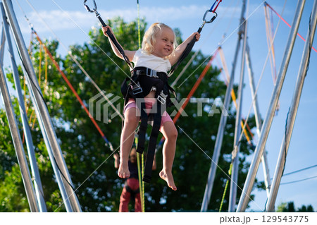 Little European Girl Learning to Jump on a Trampoline with Safety Harness. Summer Fun 129543775