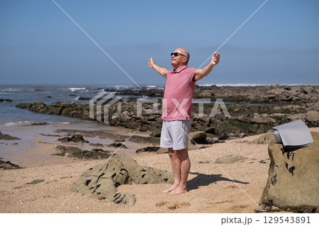 An elderly Spanish man exercising on the beach, stretching his arms. An elderly Spanish man exercising on the beach, stretching his arms. 129543891