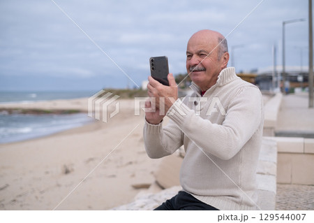 An elderly person sitting by the ocean shore, taking photos of the view.  129544007