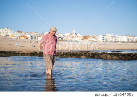 An elderly man with a mustache walking on the beach, enjoying his vacation. 129544008