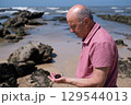 Elderly Man with Mustache Examining a Sea Urchin on the Beach 129544013