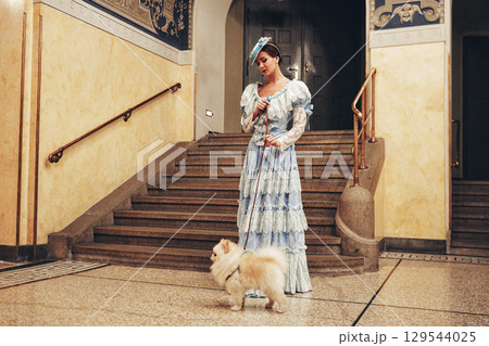 Elegant woman in blue dress with white fluffy Pomeranian dog near stairs 129544025