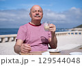 Elderly Man with Mustache Drinking Coffee at Outdoor Cafe on Vacation 129544048