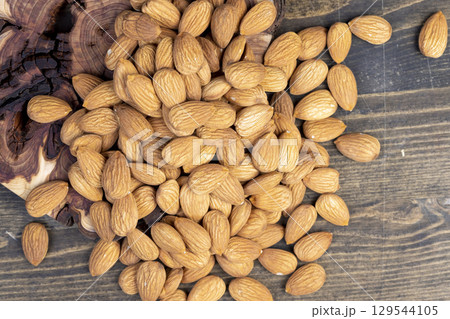 dried almonds scattered on a wooden table, edible delicious and crunchy brown almonds, closeup dried almonds scattered on a wooden table, edible delicious and crunchy brown almonds, closeup 129544105