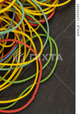 rubber bands for money packaging, scattered rubber bands of different colors for packaging and organizing paper money, objects on a black slate board rubber bands for money packaging, scattered rubber bands of different colors for packaging and organizing paper money, objects on a black slate board 129544183