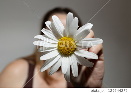 Woman Holds Daisy Flower Close to Camera With Soft Background in Warm Lighting Woman Holds Daisy Flower Close to Camera With Soft Background in Warm Lighting 129544273