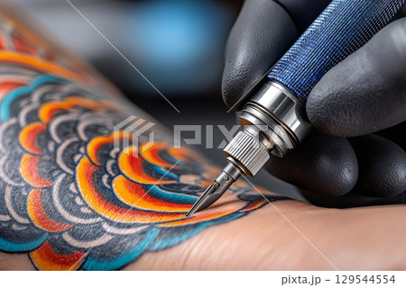 Tattoo artist applying ink with tattoo machine on client's arm Tattoo artist applying ink with tattoo machine on client's arm 129544554