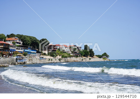 Colorful seaside houses and restaurants line the rocky coast of a picturesque village, with waves Colorful seaside houses and restaurants line the rocky coast of a picturesque village, with waves 129544710