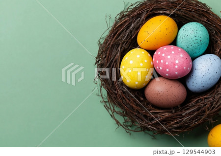 Easter eggs of different colors in a nest on a green background, top view. Festive background with copy space Easter eggs of different colors in a nest on a green background, top view. Festive background with copy space 129544903