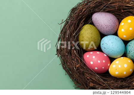 Easter eggs of different colors in a nest on a green background, top view. Festive background with copy space Easter eggs of different colors in a nest on a green background, top view. Festive background with copy space 129544904