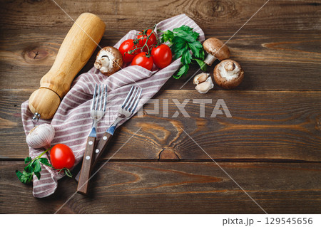 Tomatoes, garlic, champignons, parsley, pepper shaker, forks and napkin on wooden background 129545656