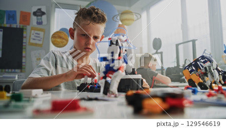 Elementary School Boy Sitting at the Desk, Examining Model of Innovative Robotic Arm 129546619