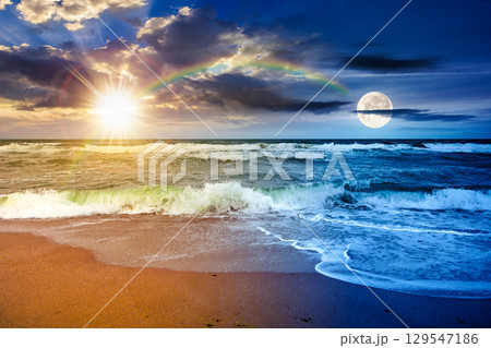 stormy beach scenery with waves splash on sand shore under scenic clouds on the sky. day and night time change concept. dark moody nature background for travel with sun and moon at twilight 129547186