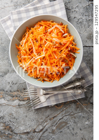 Raw carrot apple salad with raisins close-up in a bowl. vertical top view 129547295