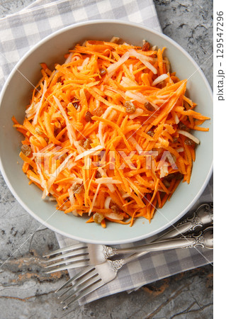 Homemade delicious carrot apple salad with raisins with lemon dressing close-up in a bowl on the table. Vertical top view 129547296