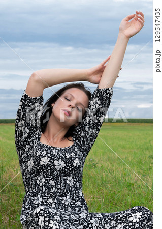 Tranquil Woman in a Floral Dress Meditating in a Field 129547435