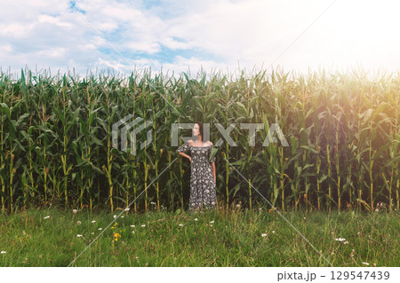 Woman Standing by Cornfield under Blue Sky 129547439