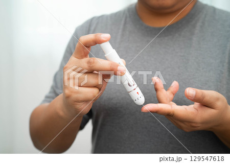 Asian woman self testing to check blood sugar level diabetes by digital lancet on finger at home. 129547618