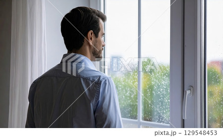 A man in a blue shirt is looking out a window. The window is foggy and the man is looking out at the city A man in a blue shirt is looking out a window. The window is foggy and the man is looking out at the city 129548453