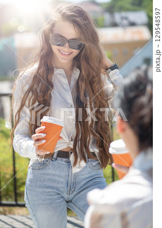 Two beautiful women having fun and drinking coffee in city during sunny summer day Two beautiful women having fun and drinking coffee in city during sunny summer day 129548597
