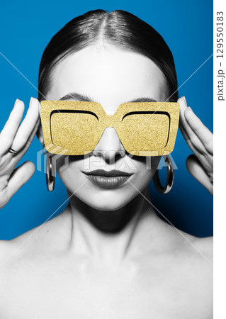 Woman portrait with classic hairstyle and golden retro sunglasses in blue background 129550183