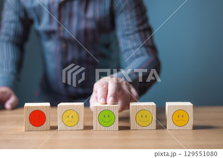 A hand selects a smiling face block among various emotion blocks, representing customer satisfaction and feedback. 129551080