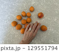 Hand with oval diamond ring arranging apricots on gray stone. 129551794