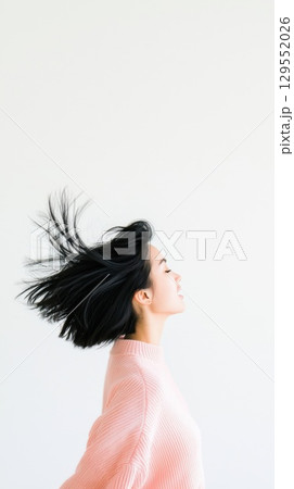 Woman in pink sweater enjoying carefree moment, windswept hair against white backdrop, expressing pure joy and liberation 129552026